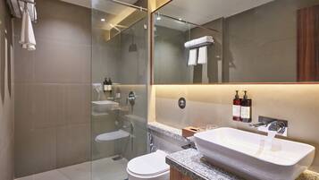 Un baño moderno con ducha de vidrio, inodoro blanco y un amplio lavabo con tocador de madera.