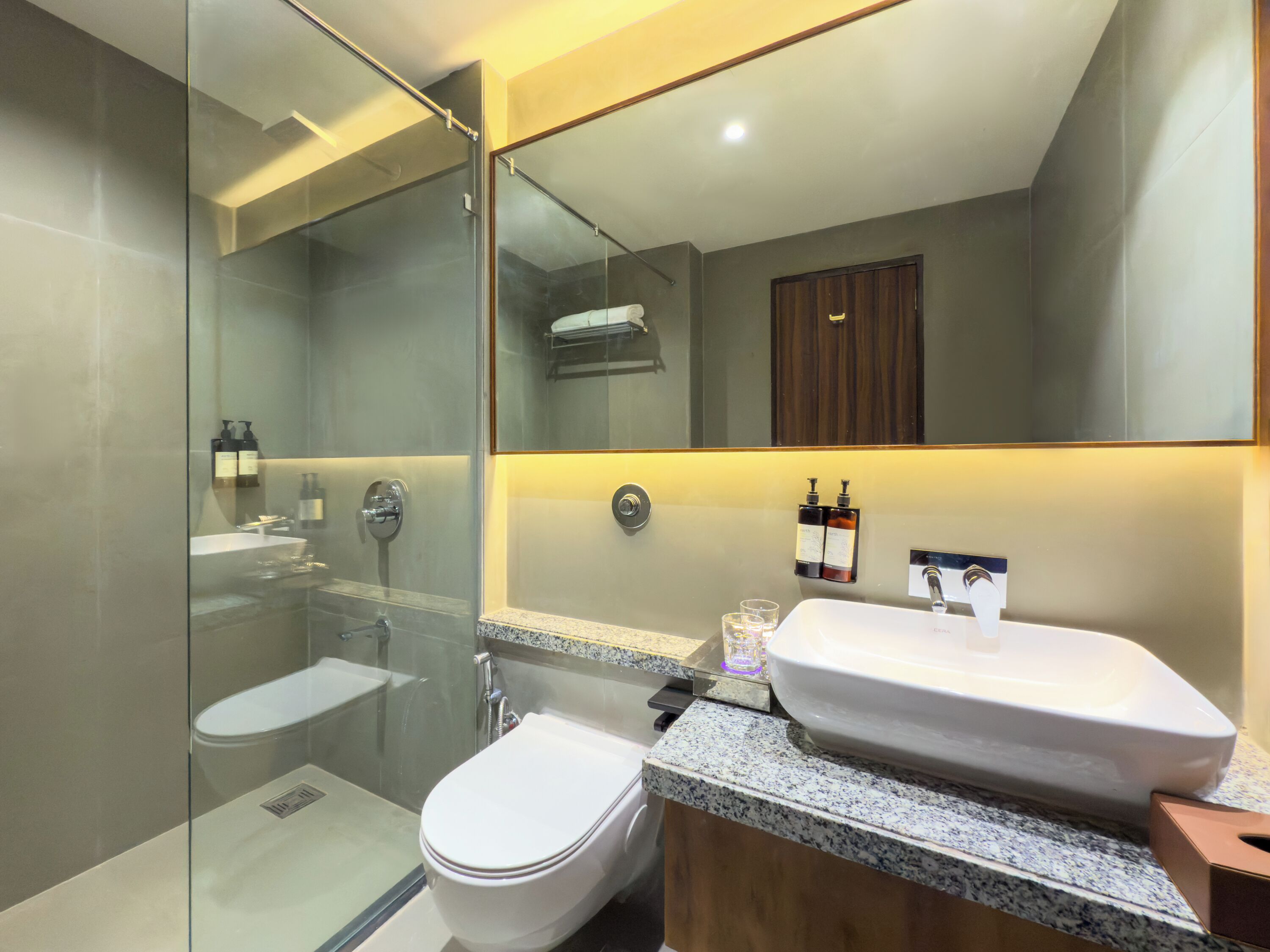 A modern bathroom with a glass-enclosed shower, a white toilet, a sink with a mirror above, and two bottles of hand soap on the wall.