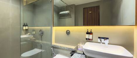 A modern bathroom with a glass-enclosed shower, a white toilet, a sink with a mirror above, and two bottles of hand soap on the wall.