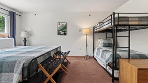 Een kleine kamer met een stapelbed, een eenpersoonsbed, een bureau en een stoel.