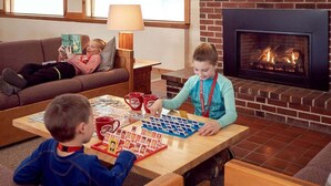 Een gezellige woonkamer met een open haard, een bank, een salontafel met een puzzel, en een kind dat met kaarten speelt.