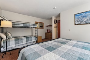 Ein Schlafsaalzimmer mit Etagenbetten, einem Schreibtisch, einem Stuhl, einer Lampe, einer Kommode und einem Poster an der Wand.