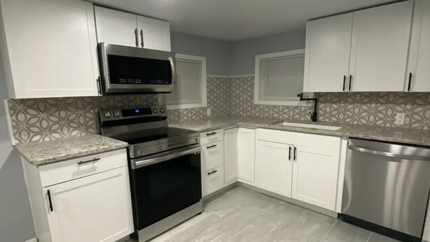 A modern kitchen with white cabinets, stainless steel appliances, and patterned backsplash tiles.