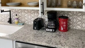 A kitchen with white cabinets, a granite countertop, a stainless steel dishwasher, a toaster, a coffee maker, and a red container.