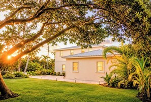Une maison à deux étages, dotée d’une pelouse bien entretenue et entourée d’arbres adultes et de plantes tropicales.