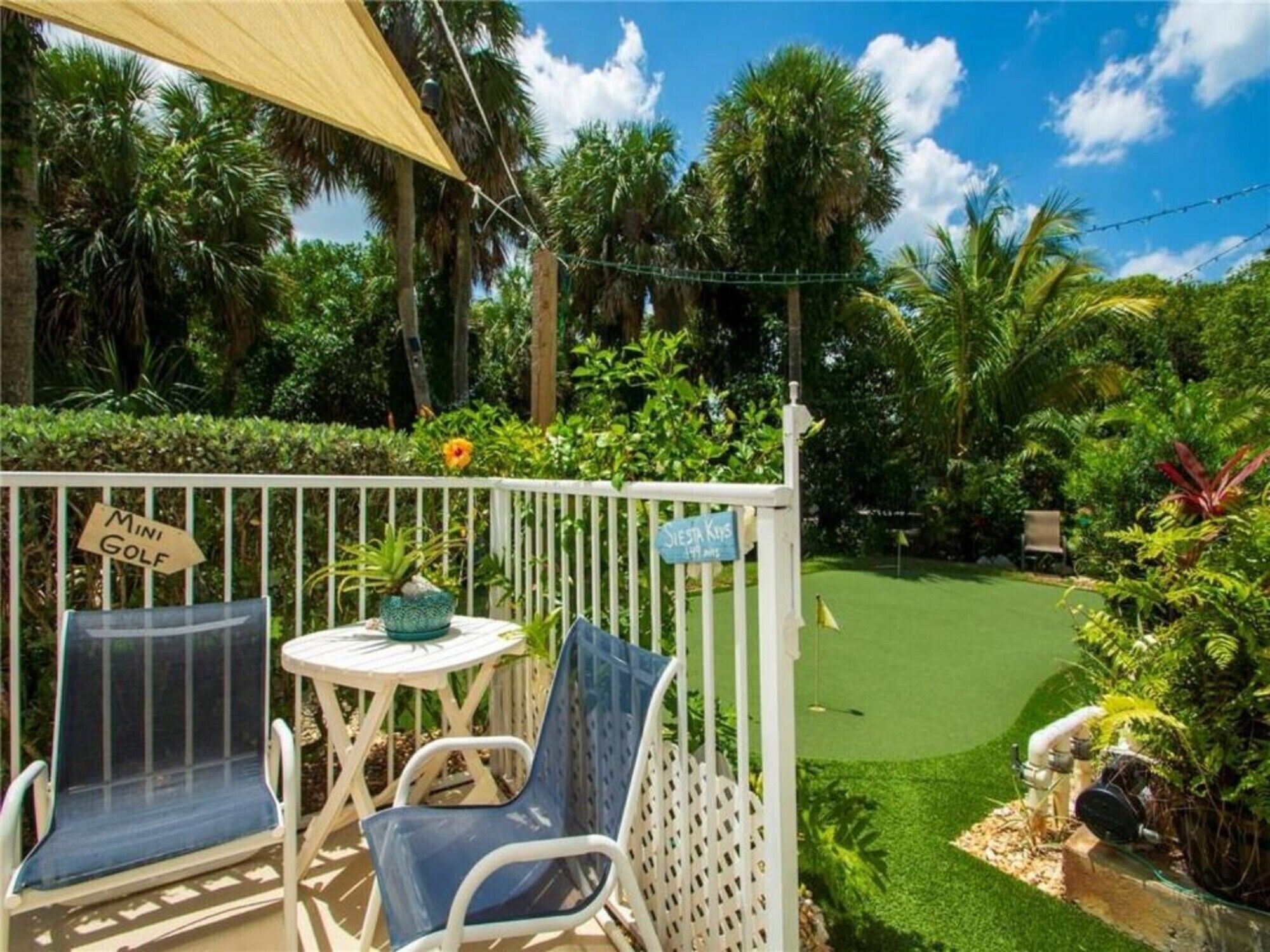 A mini golf area with two chairs and a table, surrounded by lush greenery and palm trees.