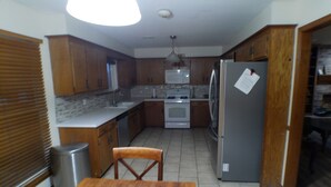 Una cocina compacta con armarios de madera, un refrigerador de acero inoxidable y una mesa de comedor con sillas.
