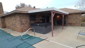 Un espacio al aire libre techado con un jacuzzi, una escalera metálica y suelo de hormigón.