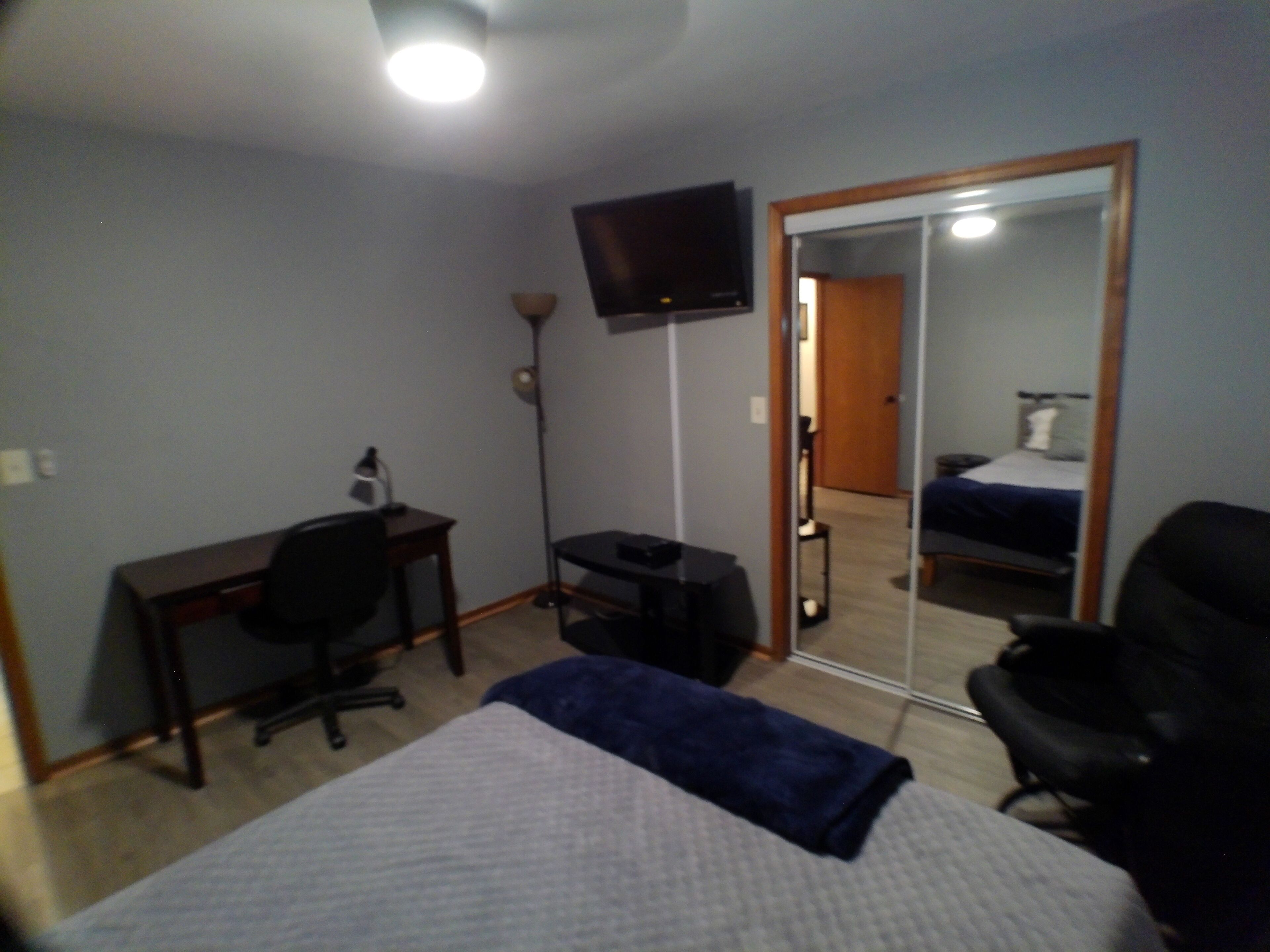 Un dormitorio con cama, escritorio, silla, televisor y espejo.