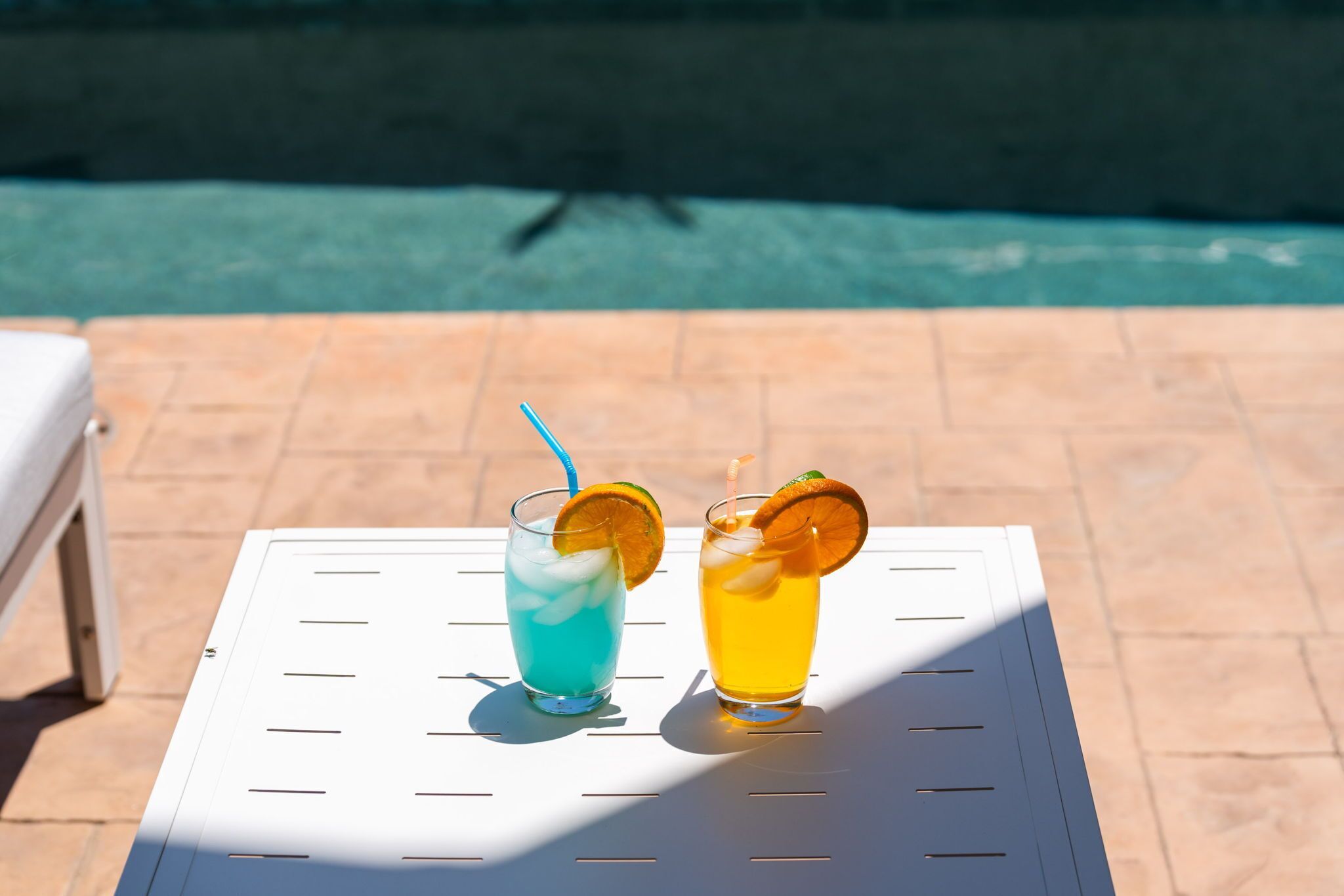 Deux boissons sur une table blanche, au bord d’une piscine.