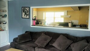 A living room with a brown sofa, a white cabinet with shelves, and a large mirror reflecting a kitchen area.