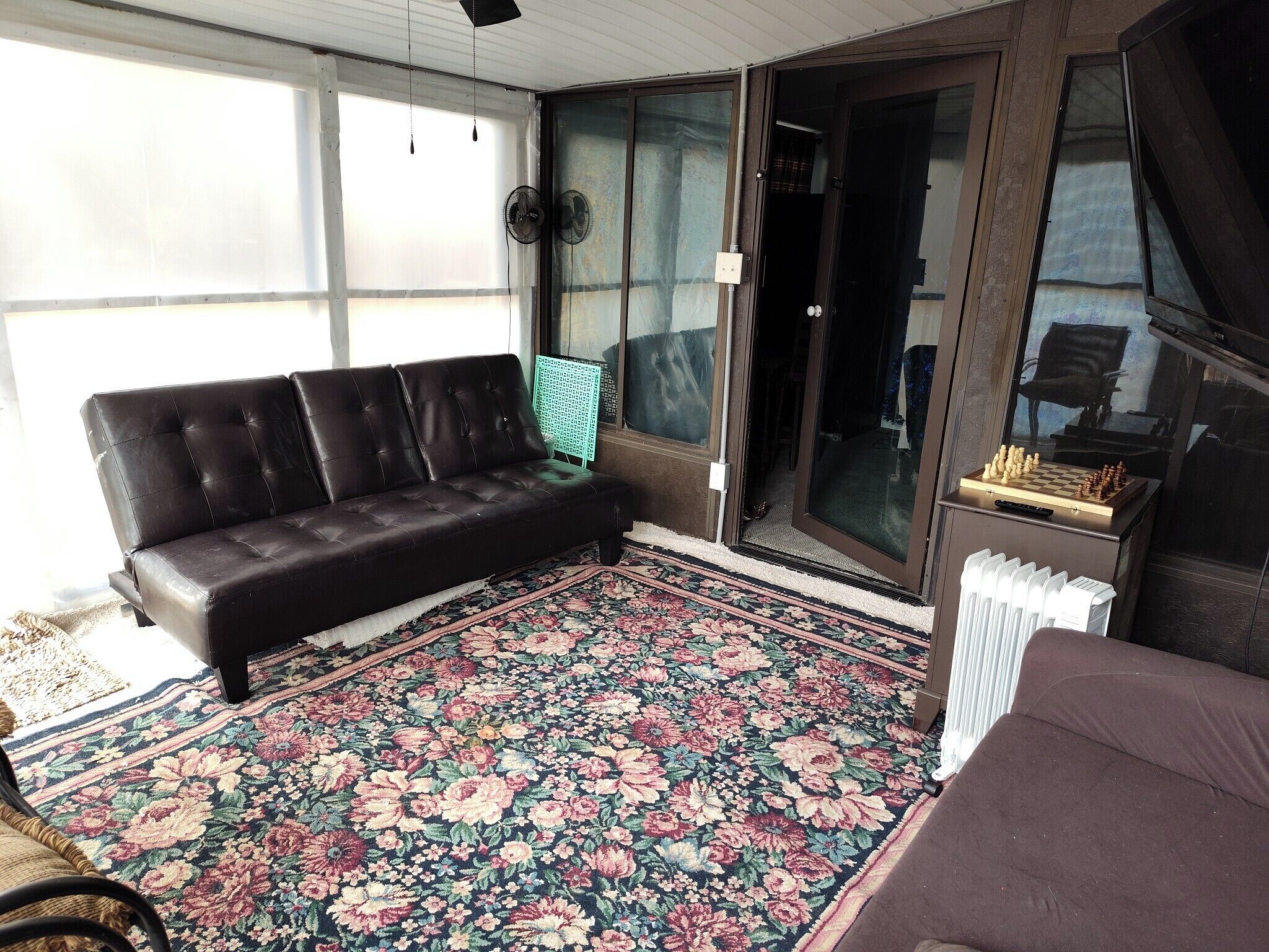 A room with a black leather sofa, a floral patterned rug, and a sliding glass door leading to a balcony.