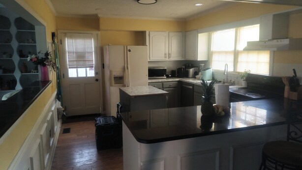 A kitchen with white cabinets, a black countertop, and a window with blinds.