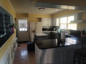 A kitchen with white cabinets, a black countertop, and a window with blinds.