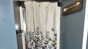 A bathroom with a shower curtain featuring a floral pattern, a towel rack, and a blue mat on the floor.