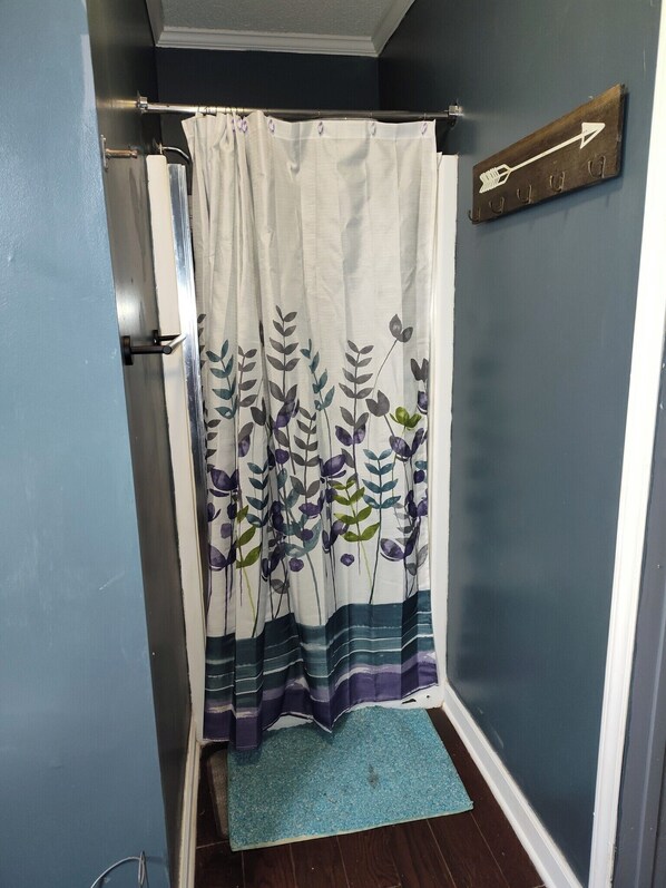 A bathroom with a shower curtain featuring a floral pattern, a towel rack, and a blue mat on the floor.