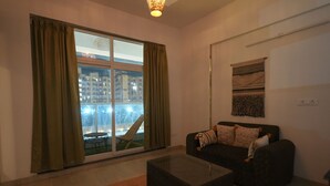 A living room with a sofa, a coffee table, and a large window with curtains. - Nimantrana (Noida)