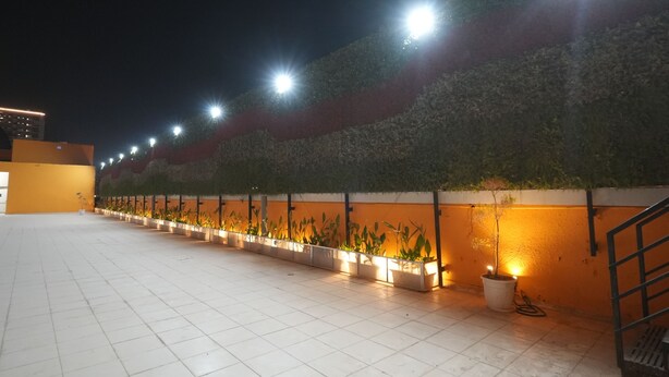 A rooftop terrace with a row of potted plants and a staircase. - Nimantrana (Noida)