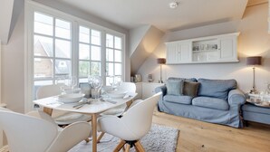Ein modernes Wohnzimmer mit Essbereich, mit einem blauen Sofa, weißen Essstühlen und einem Tisch für vier Personen.