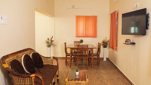 A living room with a sofa, dining table, chairs, a TV, and a ceiling fan. - RPS Service Apartment (Tiruvannamalai)