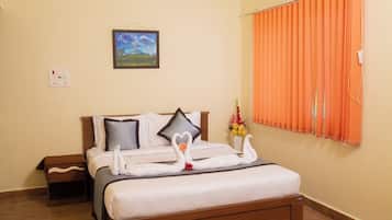 Una cama bien hecha con sábanas blancas y toallas decorativas con forma de cisne, una mesita de noche pequeña, una mesita auxiliar, un cuadro en la pared y una cortina naranja cubriendo una ventana.