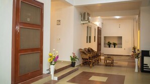 A spacious lobby with a wooden door marked G2, wicker furniture, and potted plants. - RPS Service Apartment (Tiruvannamalai)