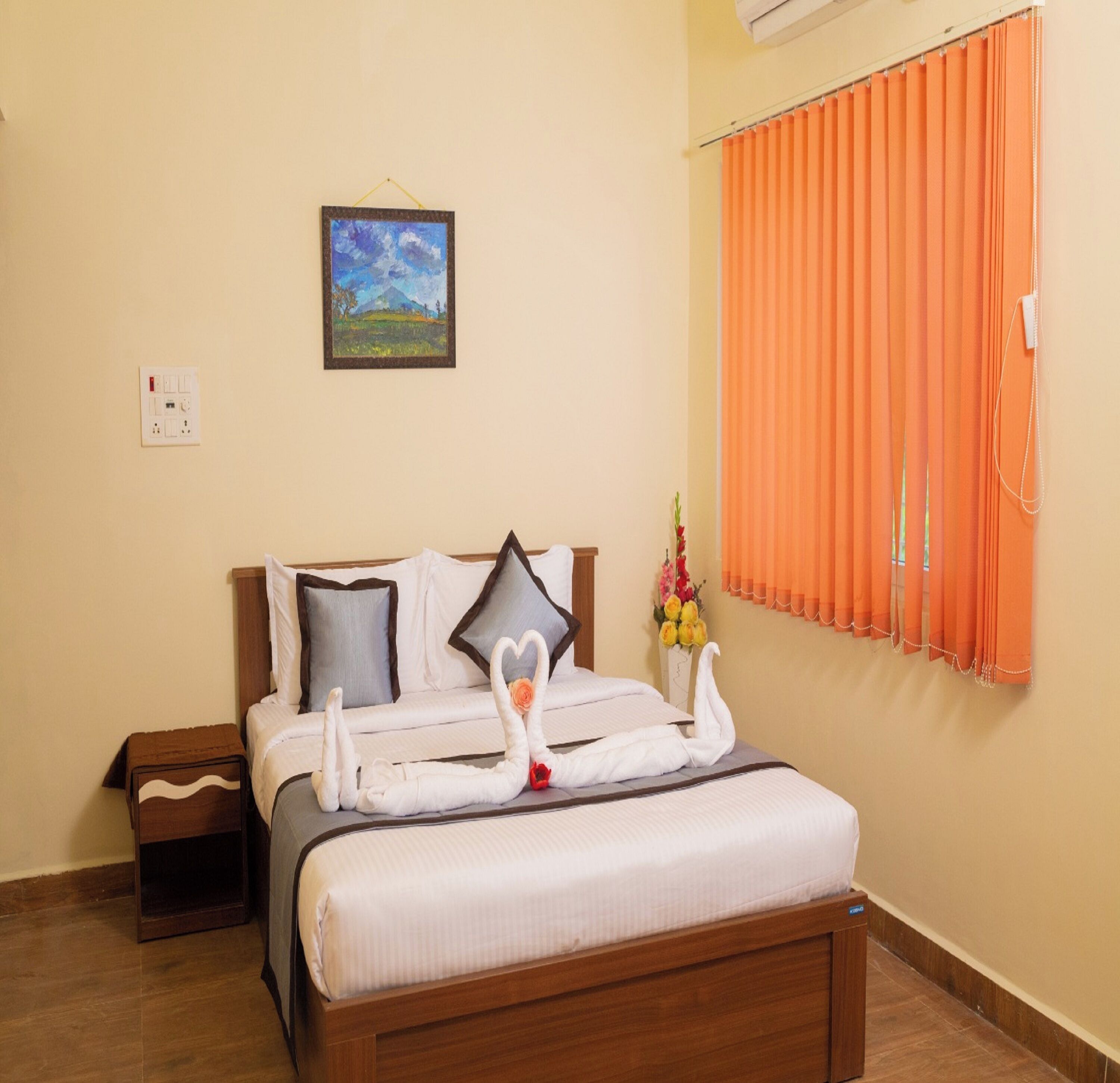 A neatly made bed with white linens and two swans made from towels, a painting on the wall, and orange curtains on the window.