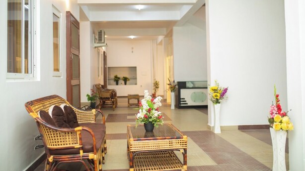 A spacious hallway with wicker furniture, a central table with a floral arrangement, and a vintage radio. - RPS Service Apartment (Tiruvannamalai)
