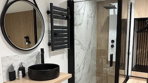 A modern bathroom with a round mirror, black sink, and wooden vanity.