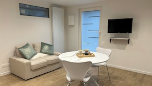 A modern living room with a beige sofa, white chairs, a marble table, and a TV mounted on the wall.