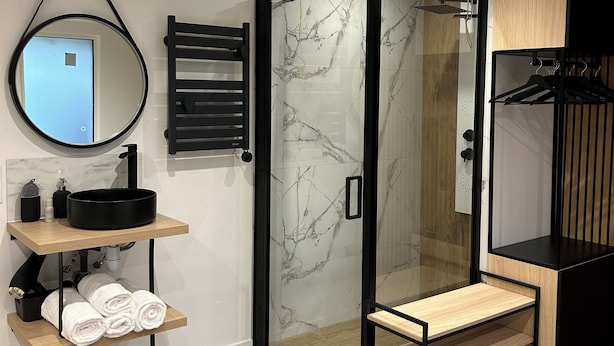 A modern bathroom with a round mirror, black sink, and a glass shower enclosure.