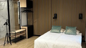 A modern bedroom with a large bed, a wooden floor, a mirror, a TV, and a camera on a tripod.