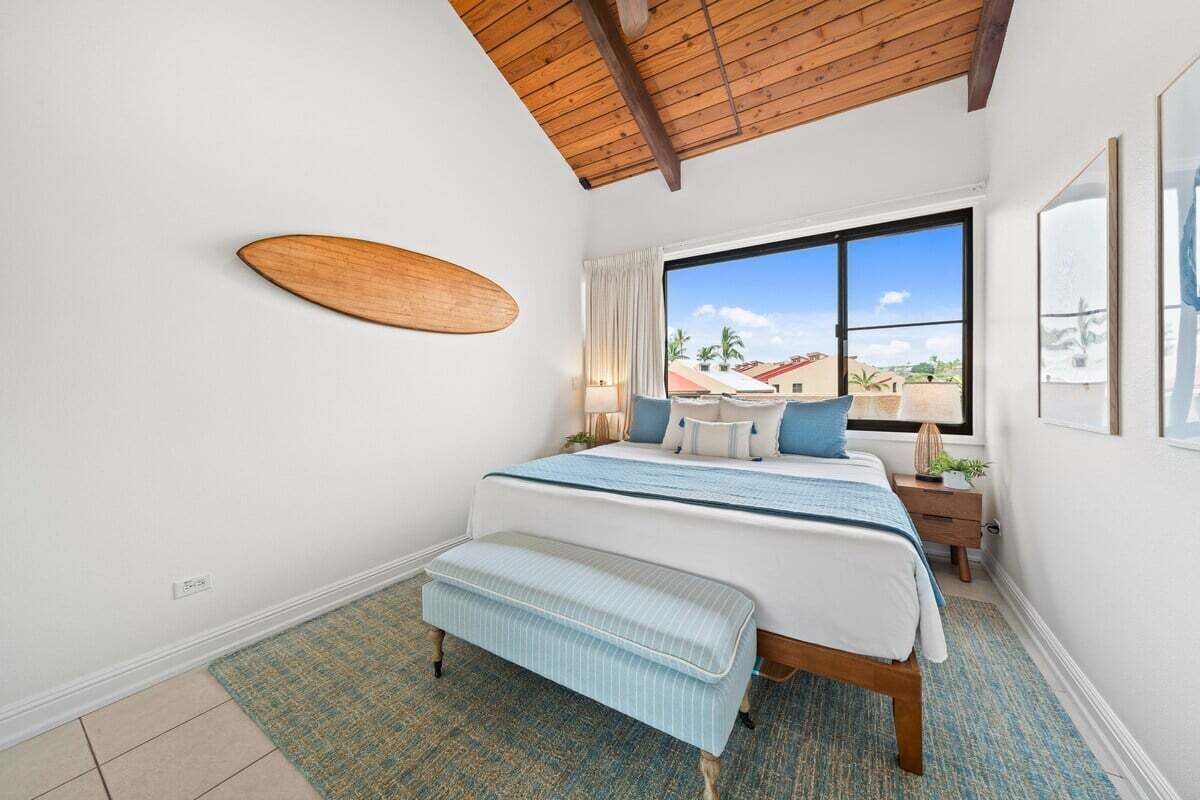 Un dormitorio con cama, banca, ventana y techo de madera.