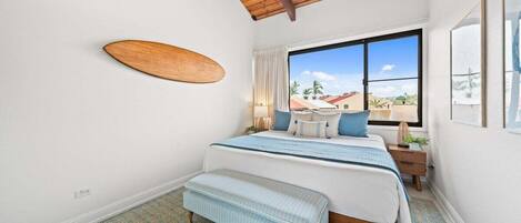 Un dormitorio con cama, banca, ventana y techo de madera.