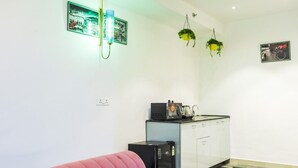 A compact kitchen with a refrigerator, a sink, and a small countertop. There are two hanging plants and two wall-mounted lights. - Nimantrana (Noida)