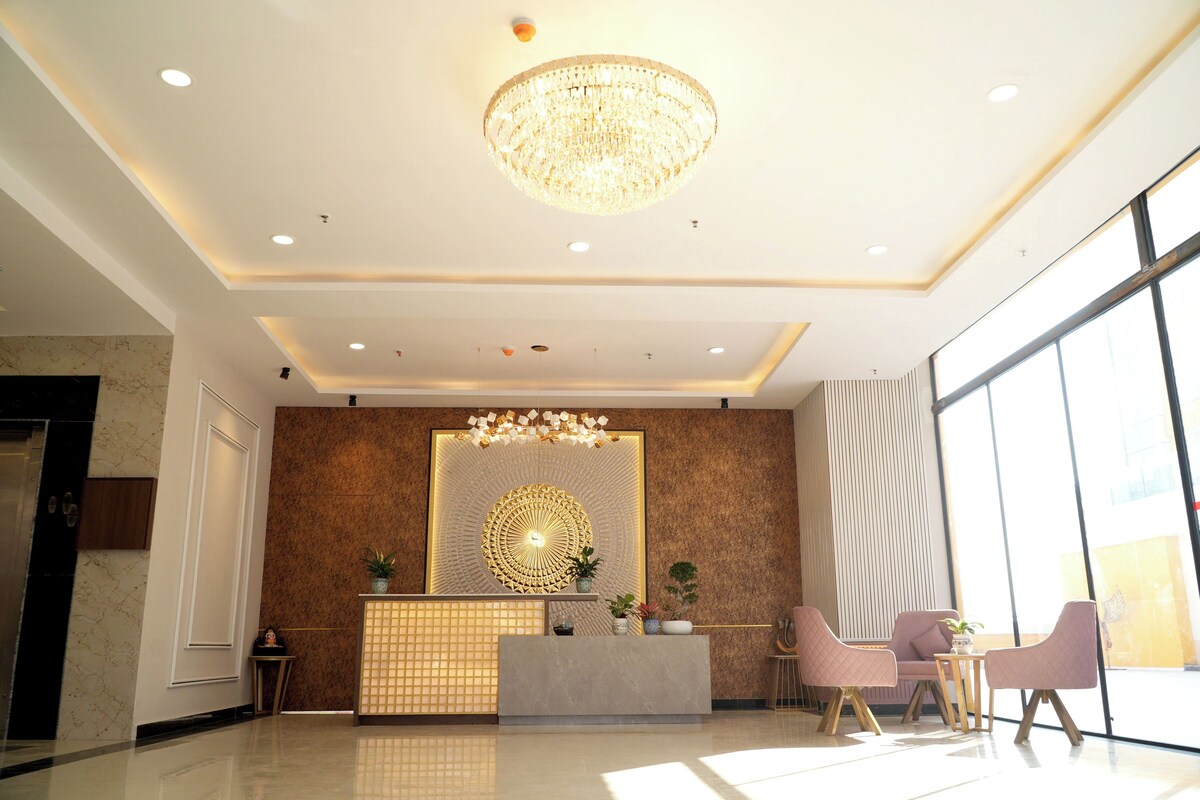 A modern reception area with a central desk, seating, and a large chandelier.