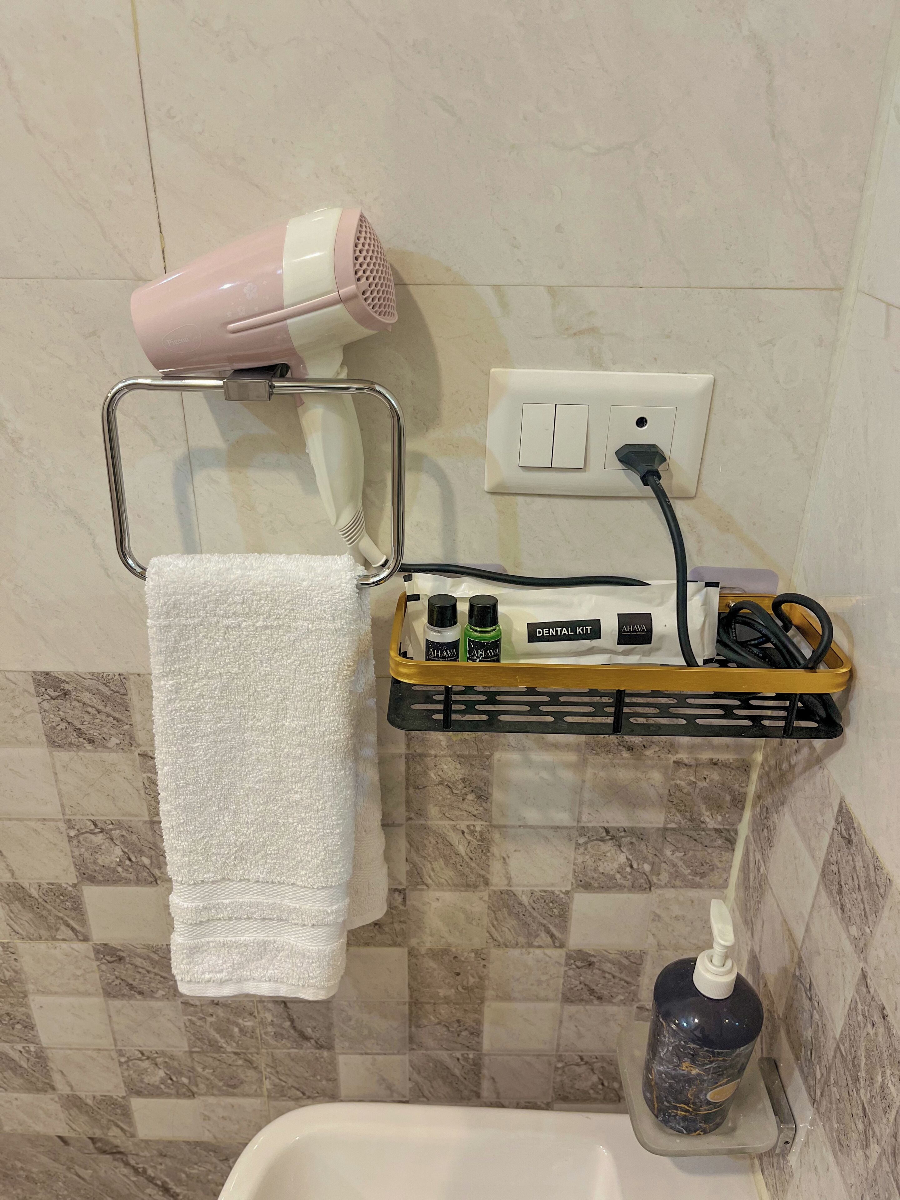 Un baño con toallero, secador de pelo, kit de higiene bucal y dispensador de jabón.