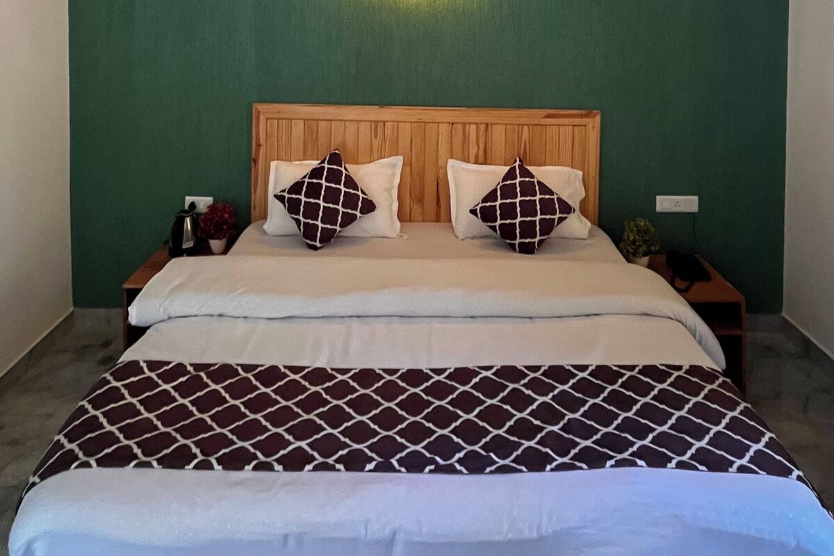 Una habitación con techo de madera, una cama con ropa de cama estampada, una mesita de noche con lámpara y una lámpara fijada a la pared.