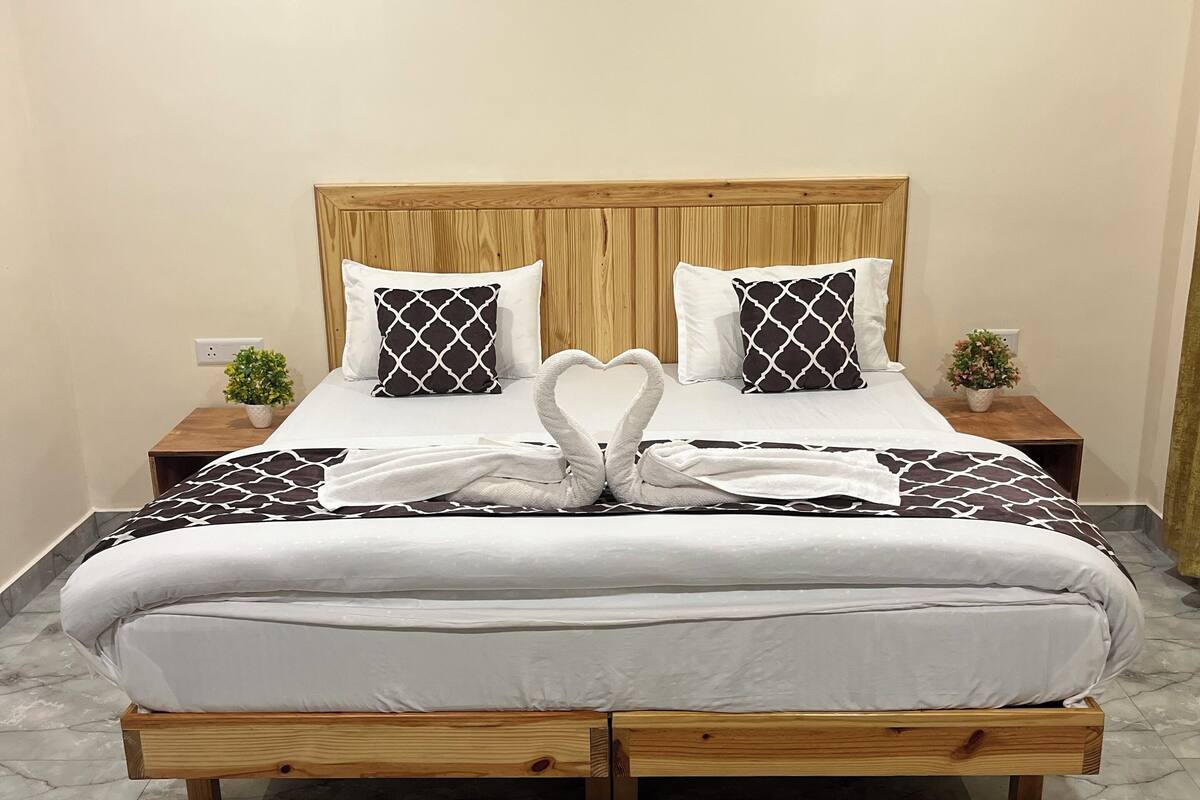 Una cama bien hecha con una disposición de toallas en forma de corazón, un cabecero de madera y un tapete decorativo.