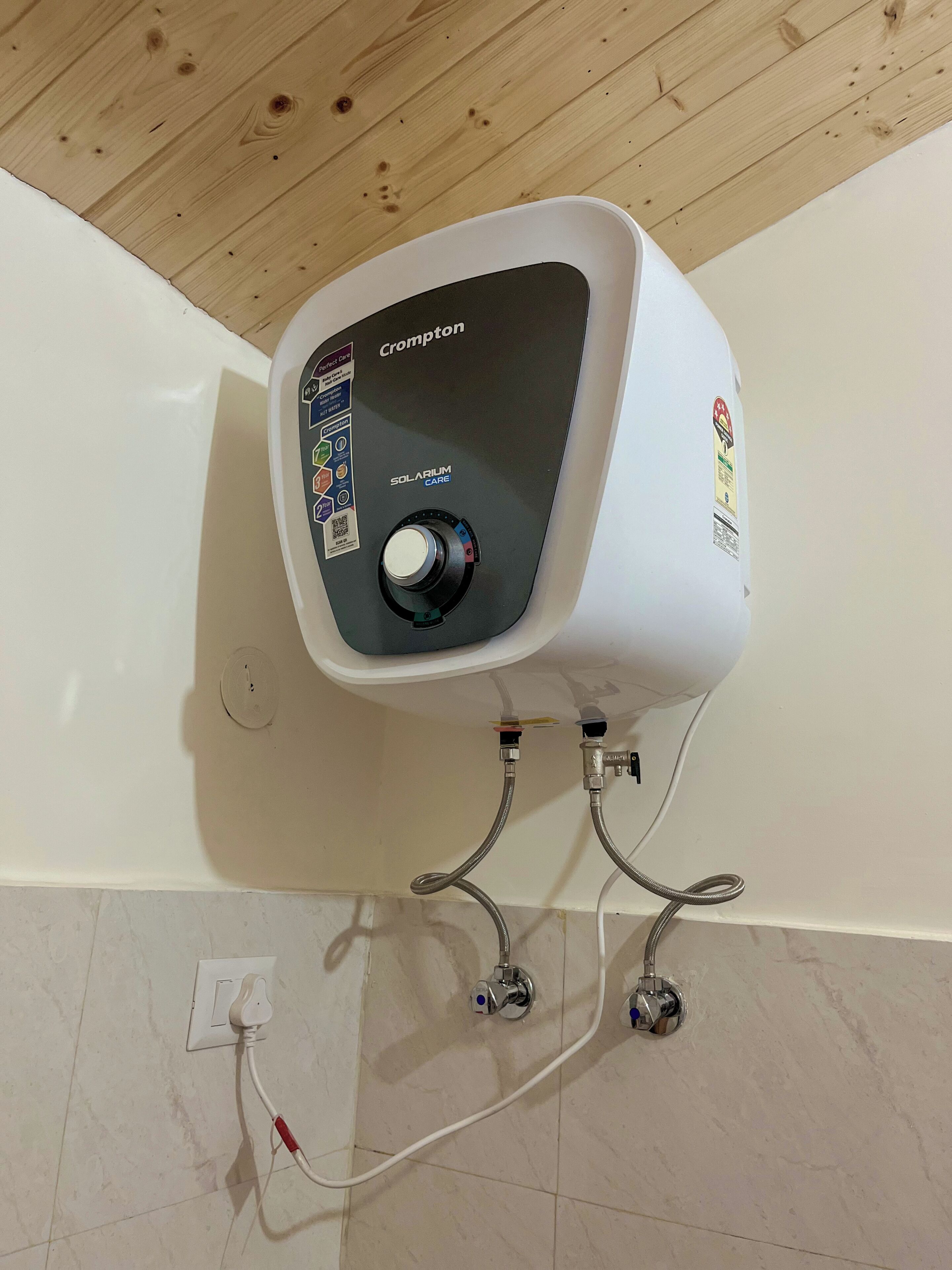 A wall-mounted Crompton solar water heater with a control panel, connected to a white wall socket.