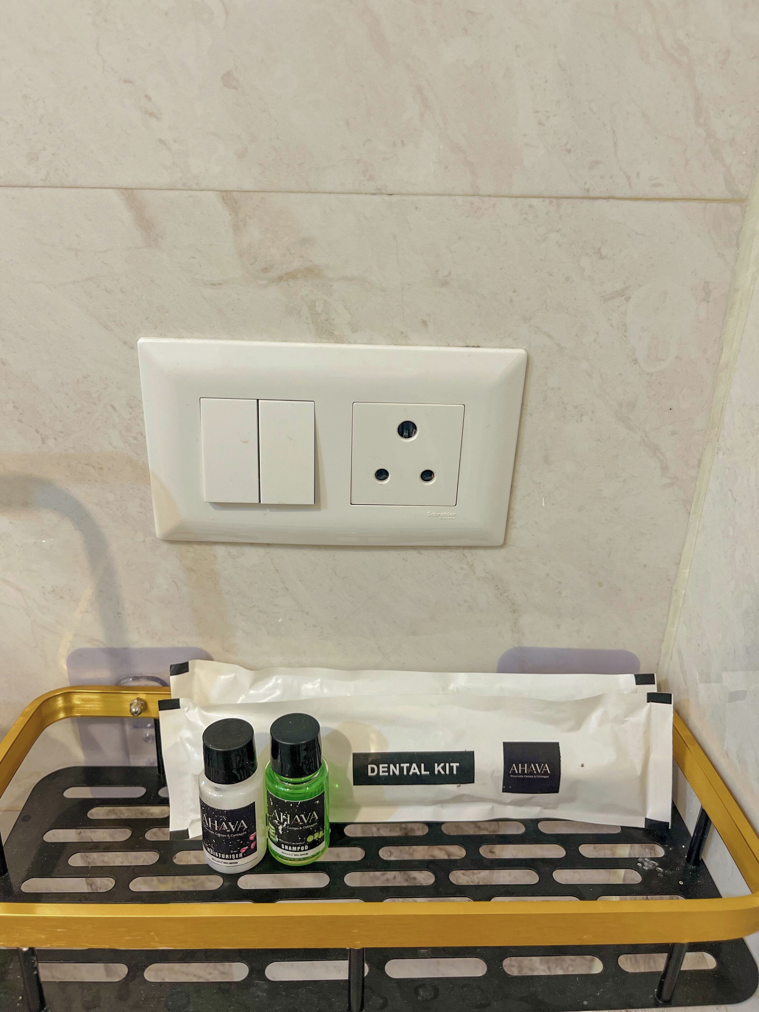 A bathroom with a white wall, a white switchboard, and a black and yellow tray with a dental kit and two bottles.
