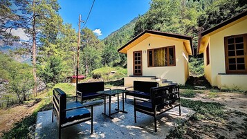 A rustic cabin with a small porch, a table with chairs, and a view of a forested hillside.