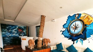 A spacious living area with a wooden floor, a reception desk, a blue sofa, and a large wall mural.