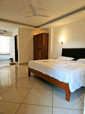 Una habitación de hotel con una cama grande, un armario, un ventilador de techo y una lámpara fijada a la pared.