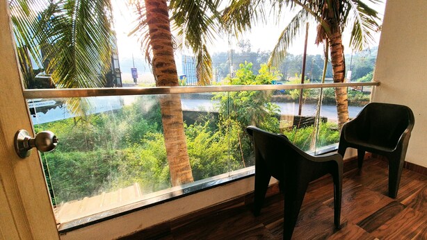A balcony with a view of greenery and a river. There are two chairs and a door with a metal handle.