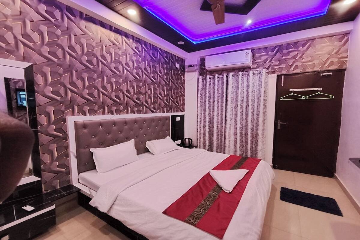 Una camera da letto moderna con testiera trapuntata, un letto rifatto con copripiumino rosso e bianco, un condizionatore d'aria a muro e una porta con attaccapanni.