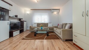 A modern living room with a flat-screen TV, a sofa, a coffee table, and a kitchen area with a fridge and microwave. - 1 bedroom gorgeous apartment in Gracac (Gracac)