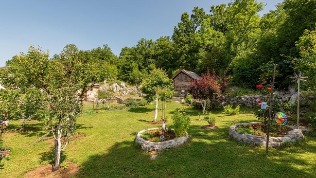 A garden with a wooden cabin, stone walls, and various plants. - 1 bedroom gorgeous apartment in Gracac (Gracac)