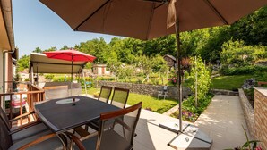An outdoor patio with a table and chairs, a red umbrella, and a view of a garden and trees. - 1 bedroom gorgeous apartment in Gracac (Gracac)