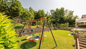 A backyard with a swing set, a stone wall, and a garden with various plants and flowers. - 1 bedroom gorgeous apartment in Gracac (Gracac)